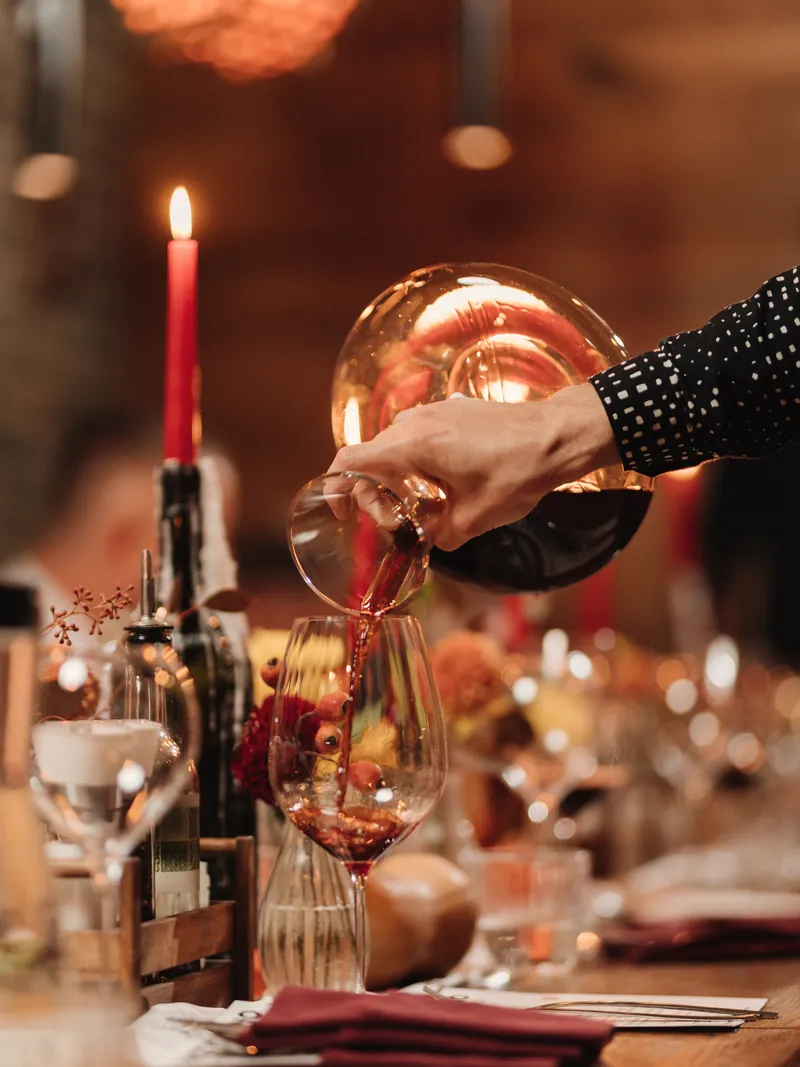 Vino rosso versato dal decanter in un calice, a una tavola apparecchiata a festa